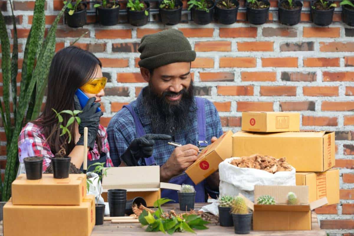 A man and a woman engaging in gardening activities, unboxing plants and gardening supplies, outdoors.