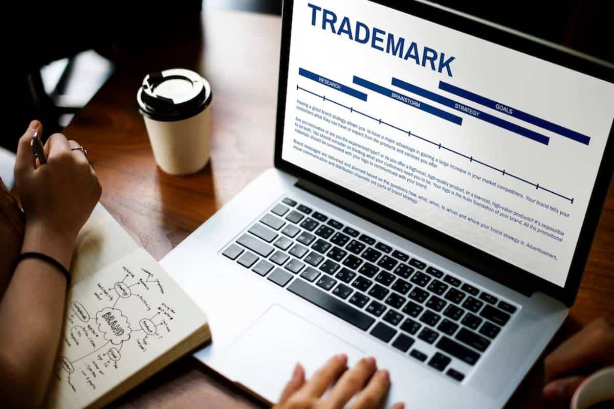 Person researching trademark strategies on a laptop with notes and coffee on a wooden desk.