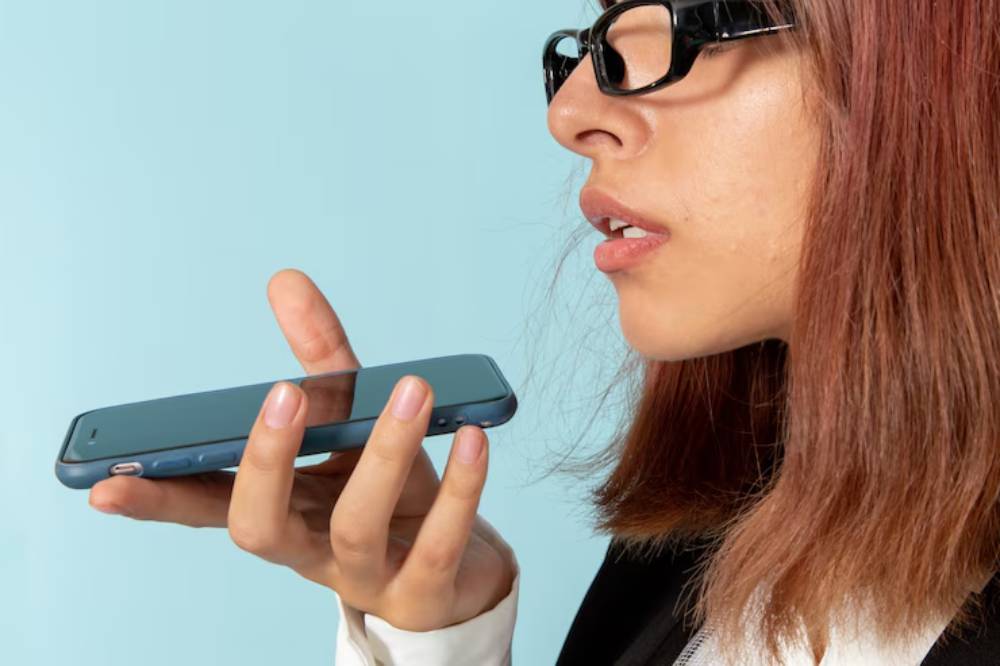 A hand holding a smartphone with a blue background, indicating voice command or voice search. 