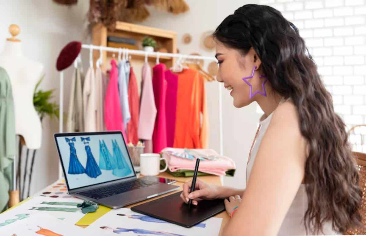 A person research products for dropshipping store on laptop, surrounded by colorful clothes in a bright workspace.