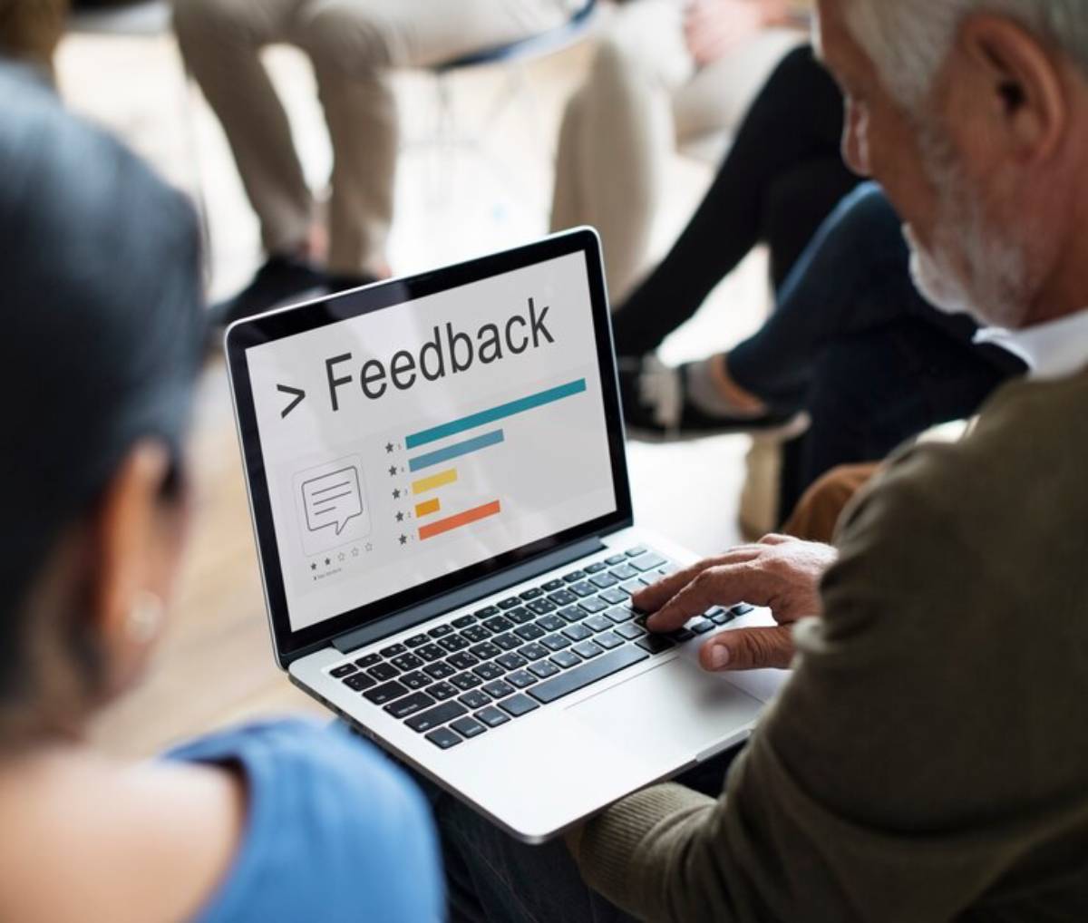 A person types on a laptop displaying a "Feedback" interface with charts and icons in a group setting.