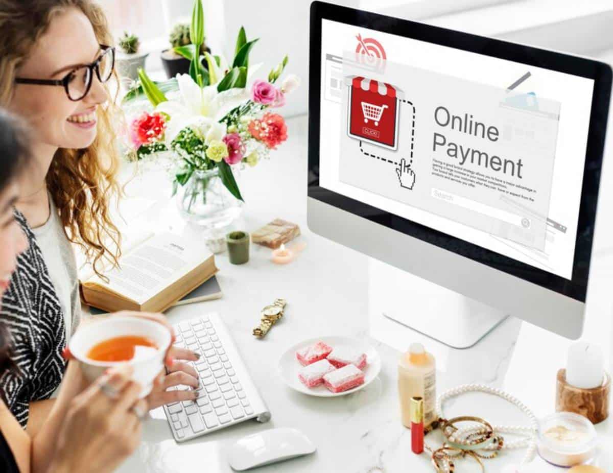 A computer screen displays an online payment interface, while a person enjoys tea and various items are spread across a stylish desk.