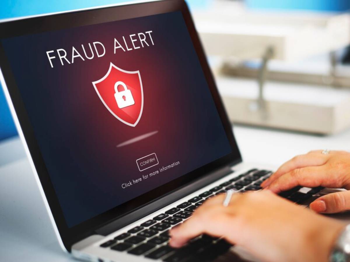 A laptop screen displaying a "Fraud Alert" message with a padlock icon, as a person types on the keyboard.