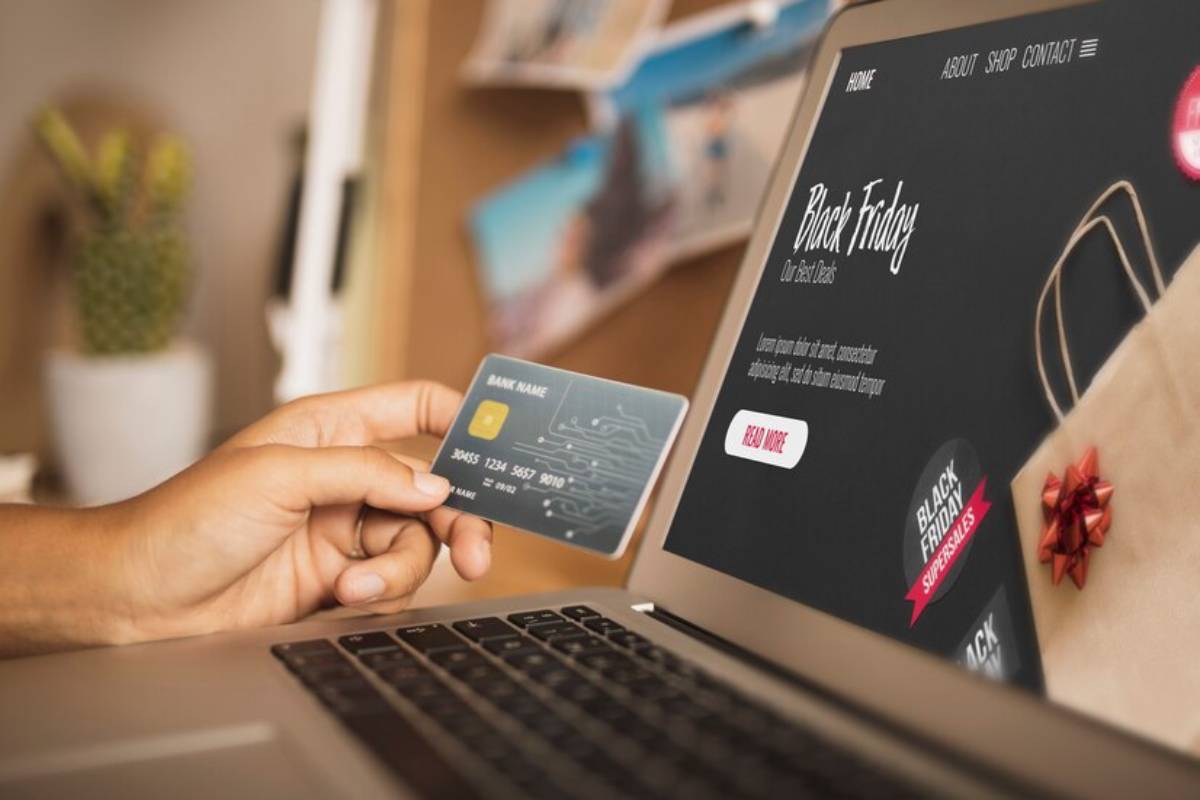 A hand holding a credit card over a laptop displaying a Black Friday online shopping webpage.