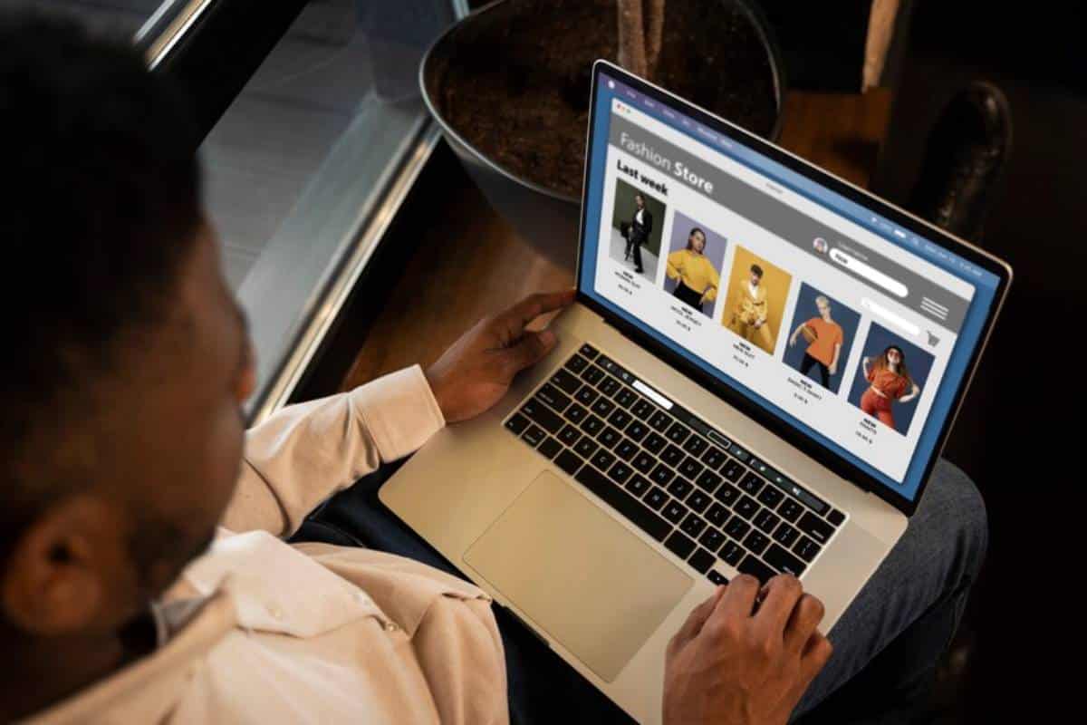 A person browsing a fashion store website, viewing clothing options on a laptop while seated near a window.