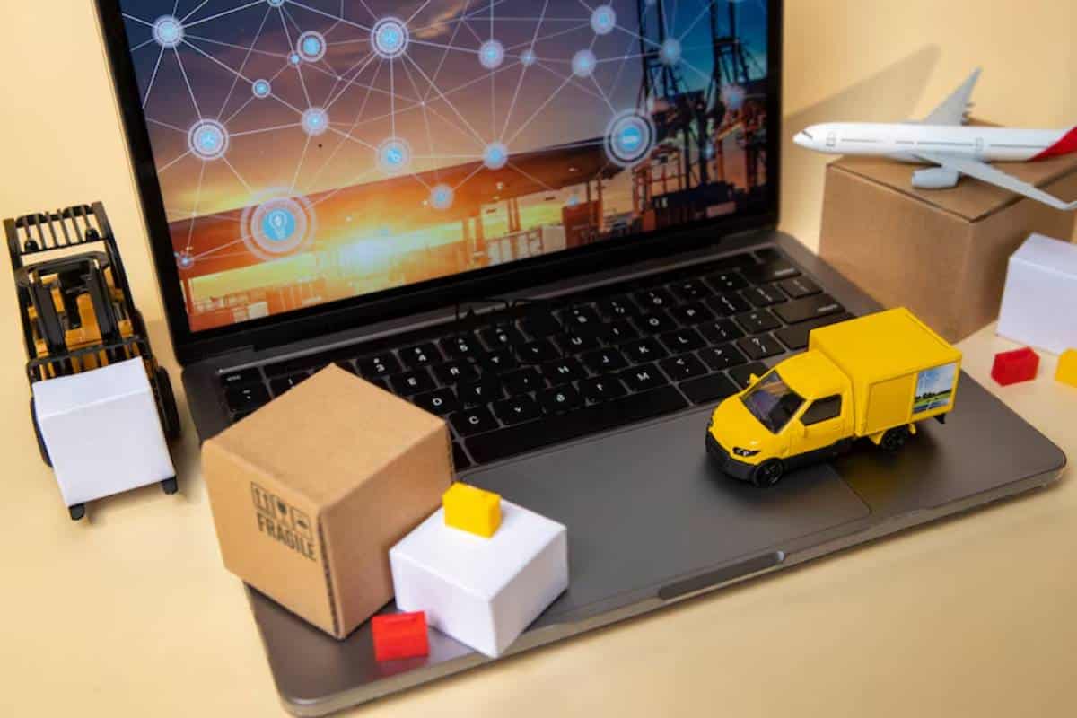 A laptop displays a logistics network, surrounded by toy vehicles, shipping boxes, and a miniature forklift, on a beige background.